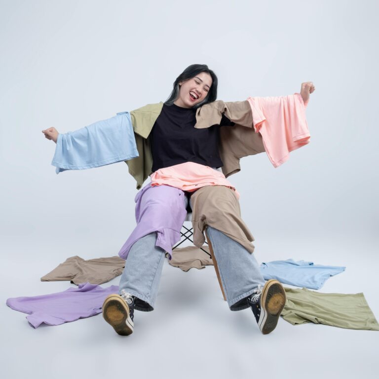 Cheerful woman sitting with a pile of colorful clothes on a white background.